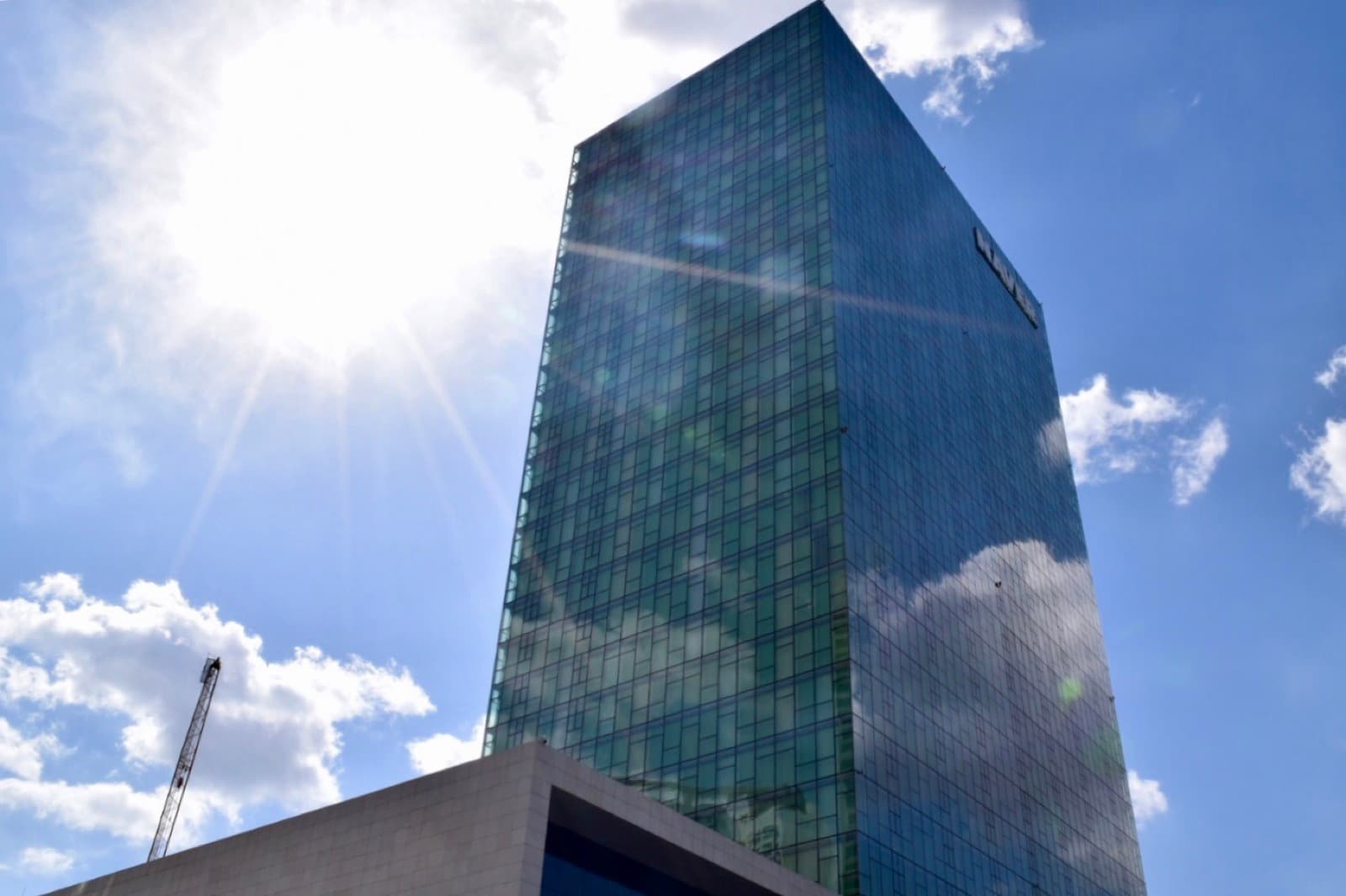Green glass skyscraper headquarters under a bright sun and blue sky
