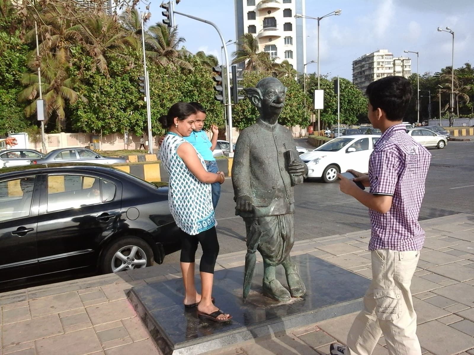 Bronze statue of the Common Man beside a busy Mumbai street, with passersby