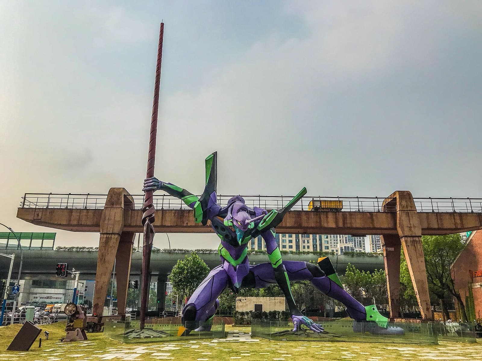 Purple and green EVA-01 robot statue holding a long spear in an outdoor plaza